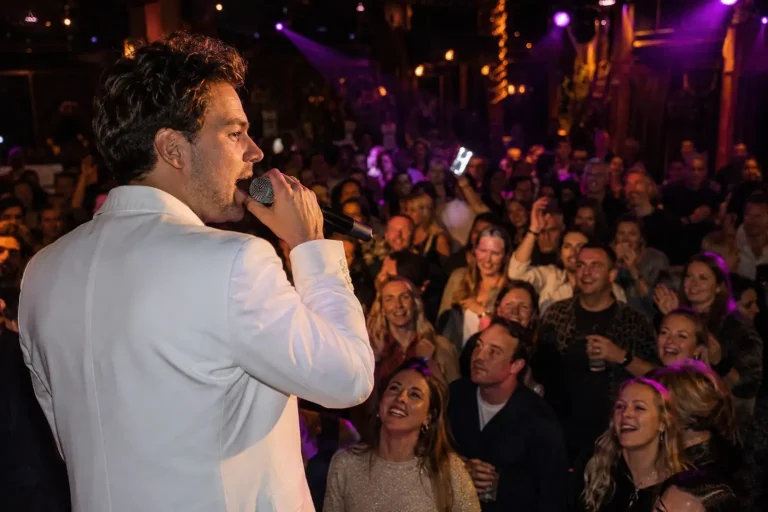Chris Riven zingt in een wit pak voor een groep feestgasten